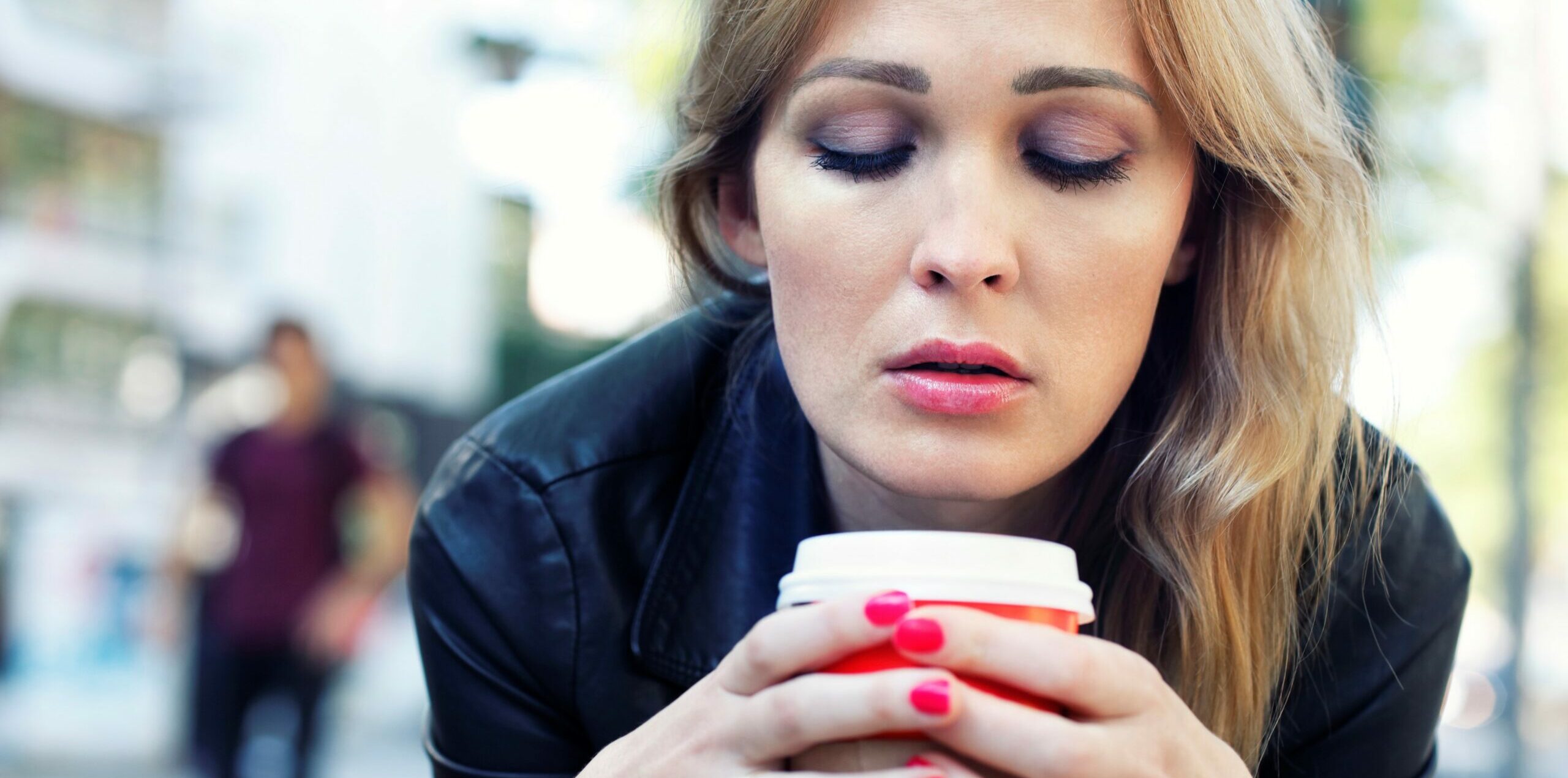 Eine junge Frau sitzt in der Fußgängerzone und schaut traurig auf ihren Coffee-to-go-Becher