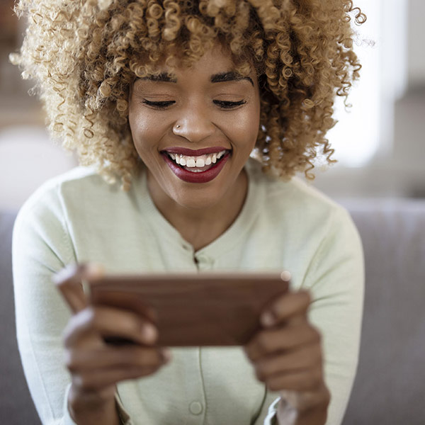 Farbige Frau schaut in ihr Smartphone und lacht freudig dabei