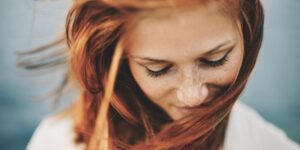 Frau mitte dreißig mit roten Haaren schaut verträumt auf den Boden.