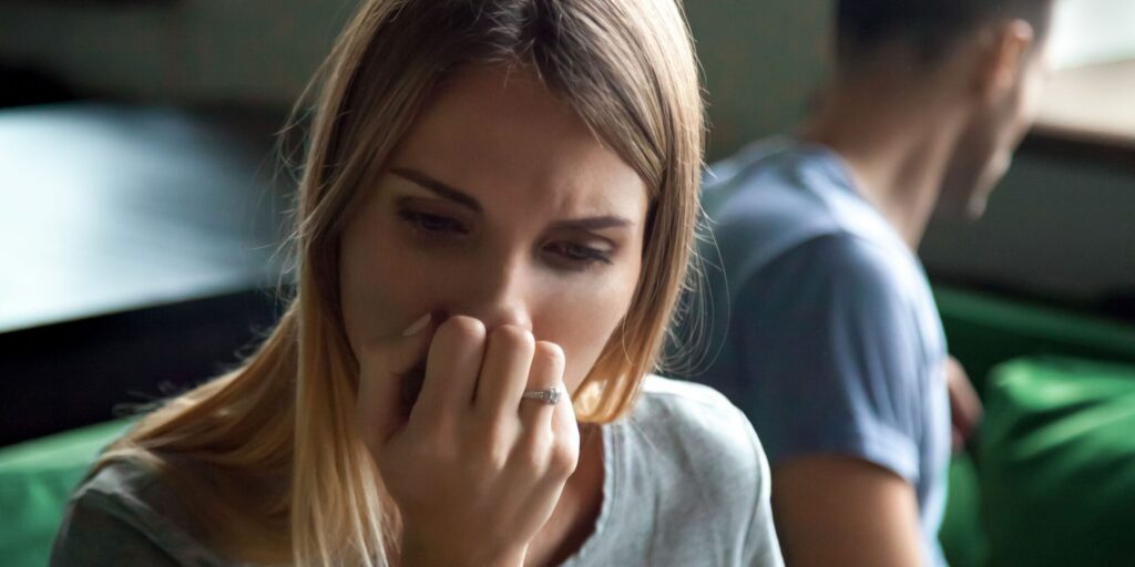 Nahaufnahme Porträt einer aufgebrachten, beleidigten, frustrierten Frau, die getrennt auf der Couch sitzt, Sofa mit Mann zu Hause, verzweifelte Frau, die ihr Gesicht mit der Hand bedeckt, Trennung, Konzept für Eheprobleme
