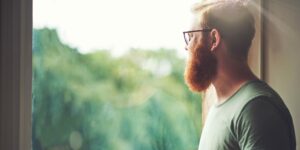 Aufnahme eines jungen Mannes, der zu Hause Kaffee trinkt und aus dem Fenster schaut