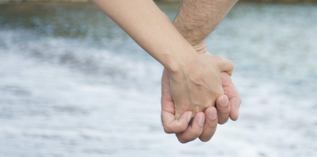Ein Paar hält Händchen am Strand. Das Bild drückt die Liebe zwischen Mann und Frau als Liebes- und Zusammengehörigkeitskonzept aus.