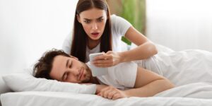 Untreue. Schockierte Ehefrau liest Nachricht von Liebhaber am Telefon, während betrügender Ehemann zu Hause im Schlafzimmer schläft. Eifersüchtige Frau überprüft Handy-Chats ihres Freundes. Affäre, Beziehungsprobleme