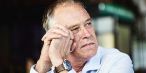 Ein nachdenklicher Mann, den Kopf auf gefalteten Händen gestützt, ist in Gedanken versunken.