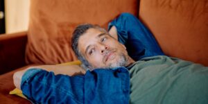 Ein Mann mittleren Alters lümmelt bequem auf einem orangefarbenen Sofa, sinniert und genießt die friedliche Auszeit zu Hause.