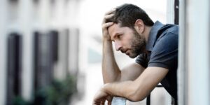 Mann mittleren alters schaut nachdenklich grübelnd aus dem Fenster