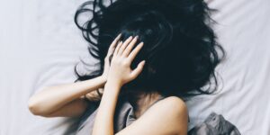 Junge Frau liegt im Bett und rauft sich die Haare