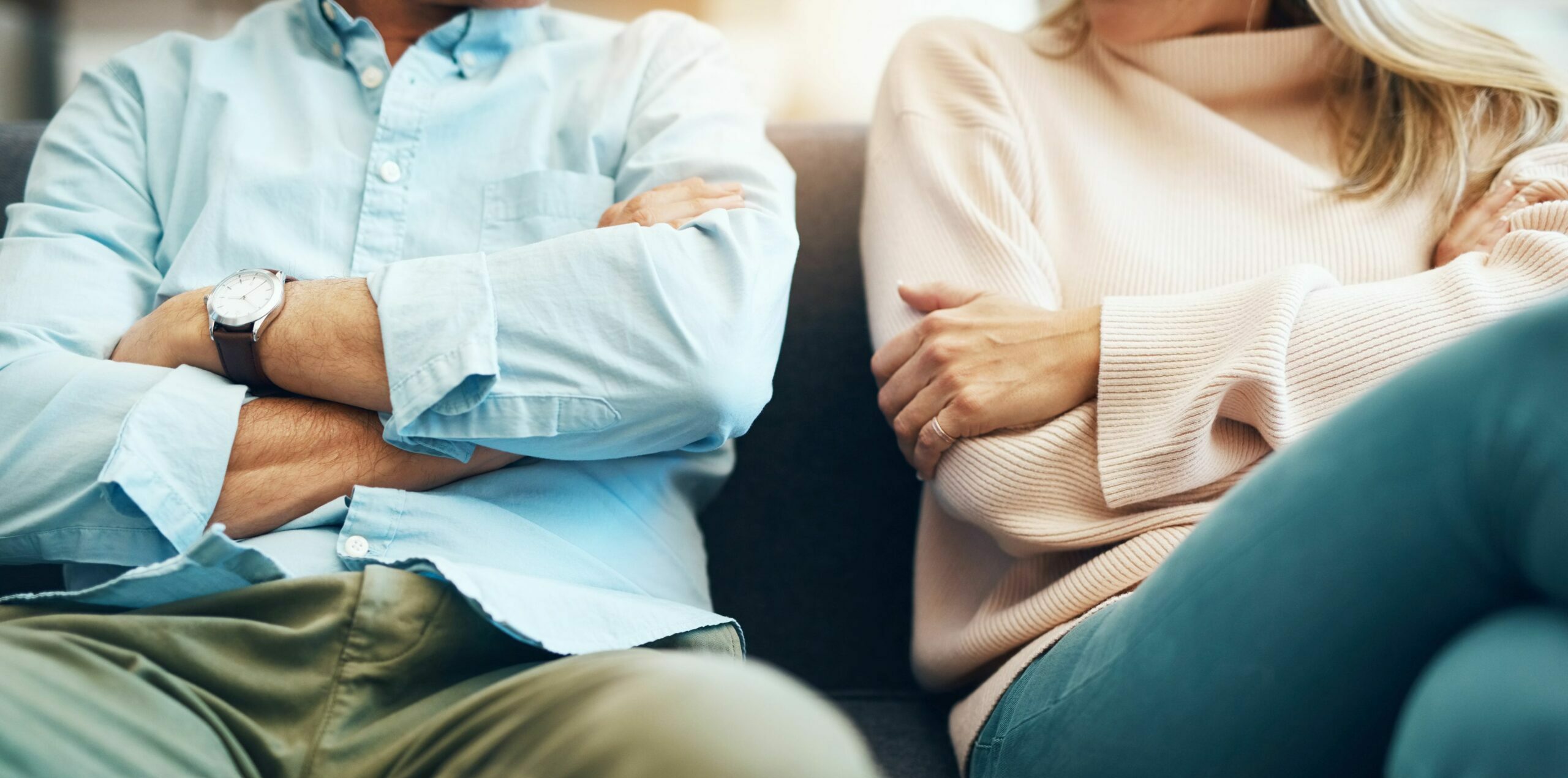 Mann und Frau sitzen mit verschränkten Armen nebeneinander auf dem Sofa