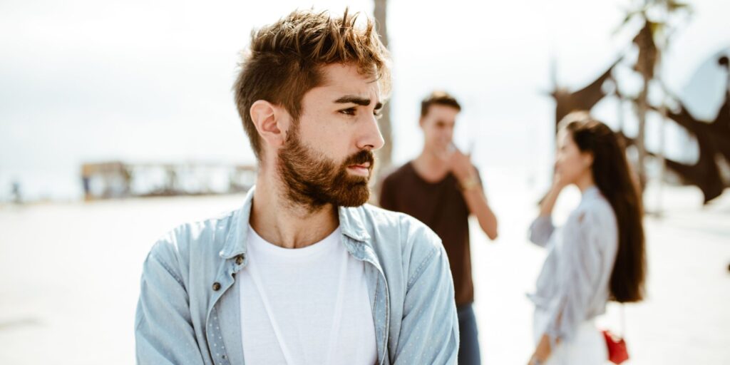 Ein Porträt eines jungen Mannes, im Hintergrund unterhält sich ein Paar