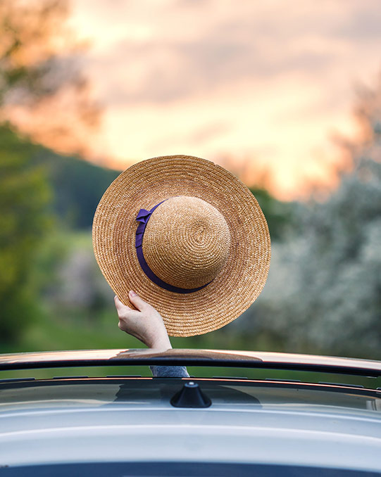 Eine Frauenhand streckt einen Sonnenhut aus dem Auto und winkt zum Abschied