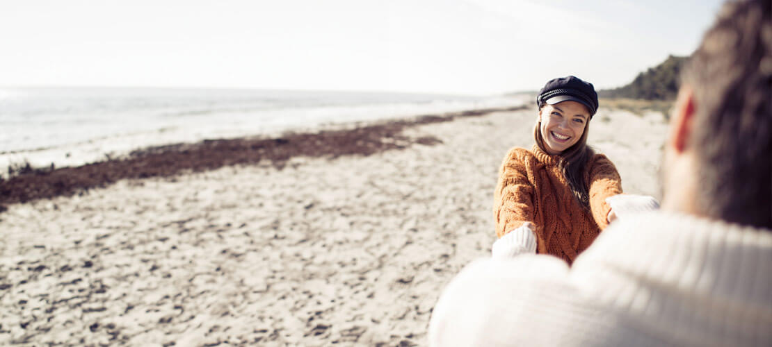 Ein Pärchen am Strand, beiden halten sich an der Hand und drehen sich.