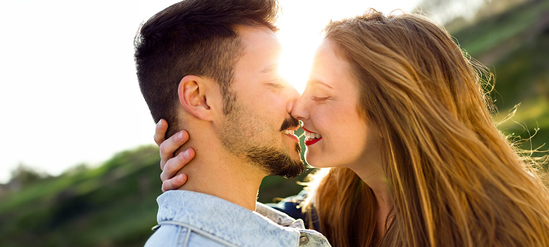 Glückliches Paar, mittleren Alters küsst sich. sie hat die Hand an seinem Hals. Fotografiert gegen die Sonne.
